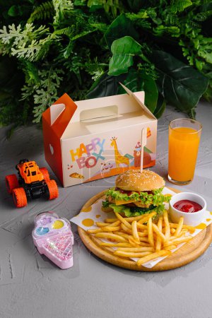 Cheerful children's meal with burger, fries, and orange juice next to a toy car and phone