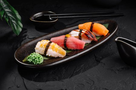 Exquisite selection of nigiri sushi served on a black plate with soy sauce and chopsticks