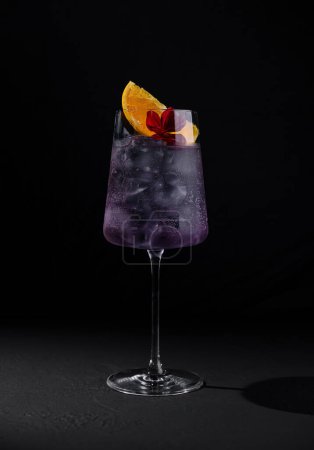 A stylish purple cocktail adorned with citrus and flower on a dark background