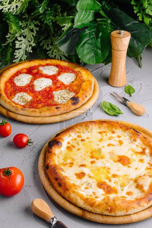 Photo for Freshly baked margherita and four cheese pizzas served on wooden boards, garnished with tomatoes and basil - Royalty Free Image