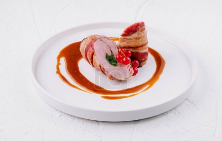 Elegant roasted pork tenderloin with red berry garnish, served on a white plate with sauce