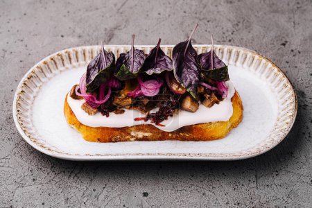 Artisanal toast topped with cream cheese, caramelized onions, and fresh purple basil on ceramic plate