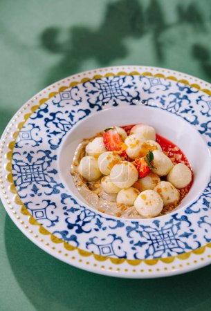 Colorful fruit salad with melon balls and strawberry slices, served in an ornate bowl on a green background
