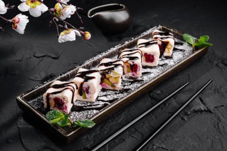 Sushis de fruits artisanaux avec sauce au chocolat sur un plateau de service en ardoise, coiffé de fleurs d'orchidée