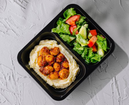 Grilled shrimp with mashed potatoes and fresh salad in a black takeout container, ready to eat