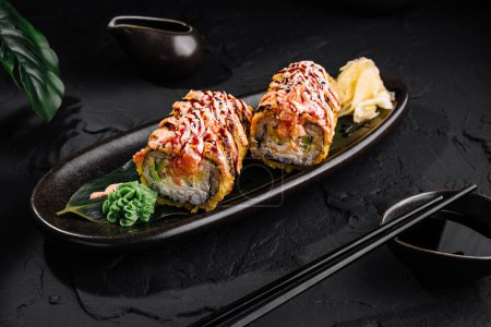 Apetyczna tempura sushi roll zwieńczona pikantnym majonezem na czarnym talerzu z pałeczkami