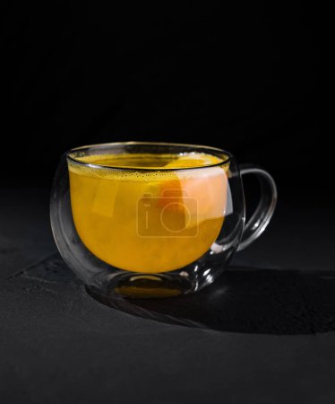 Elegant double-walled glass cup filled with hot citrus tea, highlighted against a dark background