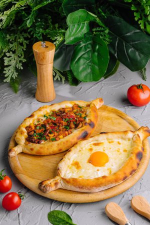Adjarian and imeretian khachapuri, served with fresh tomatoes and surrounded by herbs