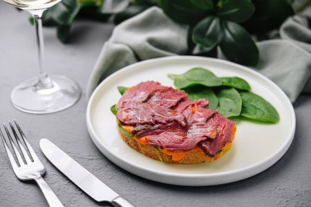 Elegant dish of sliced beef tenderloin atop a toasted bread slice and fresh spinach, presented with silverware