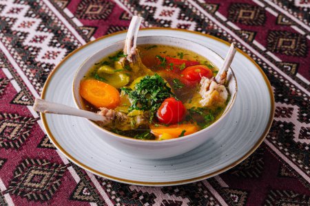 Hearty lamb soup with fresh vegetables, served in a bowl on a vibrant ethnic tablecloth
