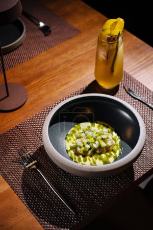 Wunderschön präsentierte Gourmet-Mahlzeit mit einem erfrischenden Cocktail an einem dunklen, stilvollen Restauranttisch