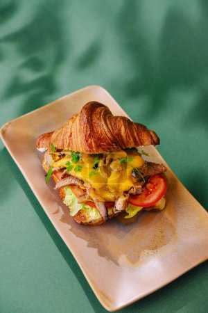 Delicioso sándwich de croissant con rellenos suculentos presentado en un plato elegante