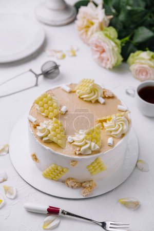 Stylish vanilla cake decorated with whipped cream swirls and honeycomb pieces on a white table