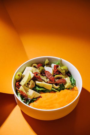 Colorful bowl of fresh vegetable salad placed on a bold orange backdrop, highlighting healthy eating