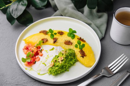 Delicious omelette with avocado, salsa and herbs on a white plate, with coffee