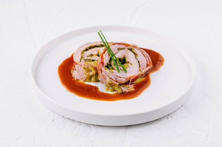 Elegante roulade de cerdo lleno de hierbas y servido con una rica salsa marrón en un plato blanco