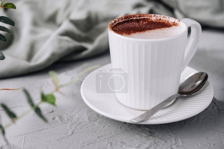 Scène confortable avec une tasse blanche de cappuccino avec de l'art de la mousse, aux côtés d'une cuillère et de verdure
