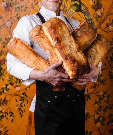Photo for Professional baker in an apron proudly presents a selection of golden brown baguettes - Royalty Free Image