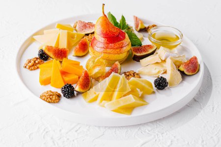 Agencement élégant de différents fromages, figues fraîches, poires et noix sur une assiette en céramique