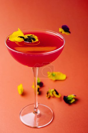 Vibrant cocktail decorated with edible flowers, presented in a stemmed glass against a warm-toned backdrop