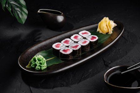 Schön arrangierte Thunfisch-Sushi-Rolle auf Blatt, mit Ingwer und Wasabi, auf glatter schwarzer Oberfläche