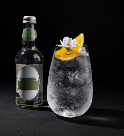 Elegante ginebra y bebida tónica adornada con rodaja de limón y flor sobre fondo oscuro