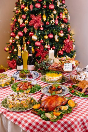 Holiday table laden with roasted turkey, sides, and desserts with a beautifully adorned christmas tree in the background