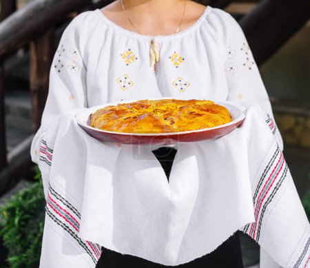 Nahaufnahme eines frisch gebackenen Biskuitkuchens, präsentiert von einer Frau im bestickten Kleid