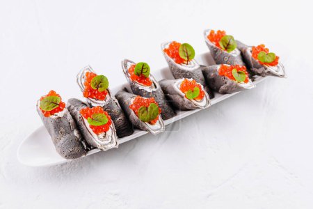 Elegante schwarze Crêpes mit Frischkäse gefüllt und mit rotem Kaviar und frischen Kräutern belegt