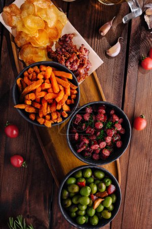 Elevated view of savory snacks including nuts, chips, and olives, presented on a rustic table