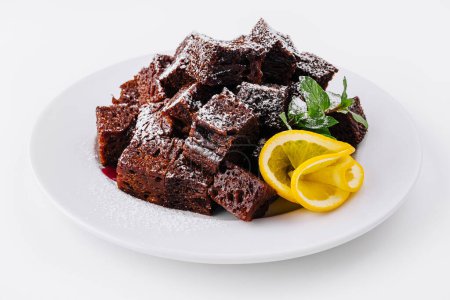 Plate of freshly baked chocolate brownie cubes, dusted with powdered sugar, garnished with lemon and mint