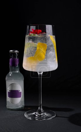 Sophisticated gin and tonic in a tall glass, accompanied by a bottle, garnished with citrus and a red flower