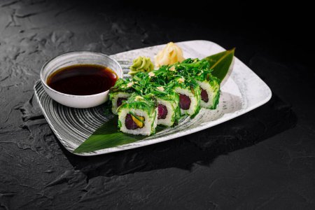Gourmet tuna sushi roll garnished with green herbs served with soy sauce on a modern plate