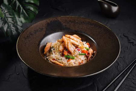 Herzhafter gebratener Reis aus Hühnerfleisch auf einem stilvollen dunklen Teller, perfekt für ein Gourmet-Menü