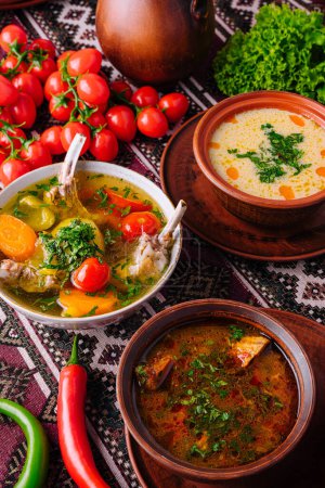 Herzhafte Schalen mit hausgemachter Suppe mit frischem Gemüse und Kräutern auf einer ethnischen Tischdecke