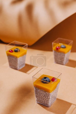 Three chia pudding desserts with mango puree garnished with berries, stylishly presented