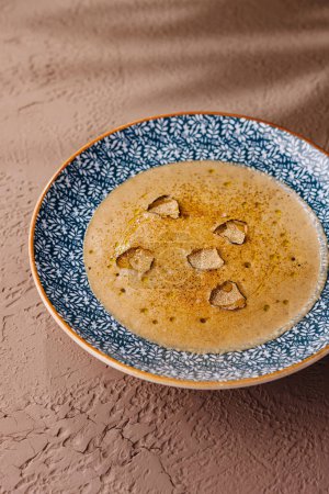 Élégant bol de soupe lisse et mélangée garnie de tranches de truffe, sur fond texturé