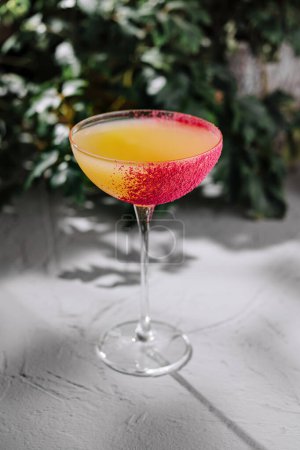 Sophisticated cocktail in a stemmed glass with a vibrant red rim, presented on a textured gray surface