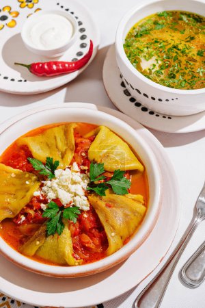Vibrant bowl of spicy soup served with stuffed peppers, garnished with fresh herbs and cheese