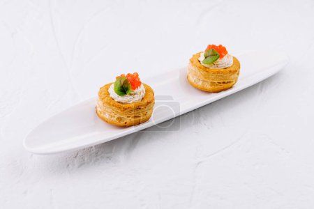 Photo for Elegant puff pastry vol-au-vent filled with cream and topped with salmon roe on a white platter - Royalty Free Image