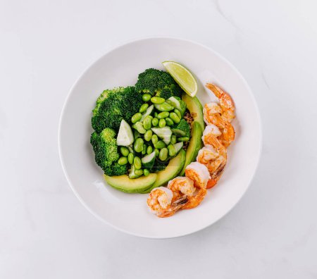Fresh green salad with shrimp, broccoli, avocado, and lime on a white background