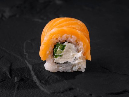 Close-up of a delectable salmon sushi roll with creamy filling and cucumber on a dark slate plate