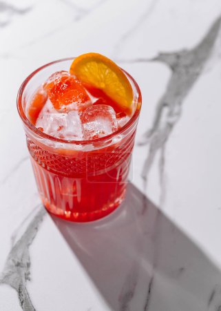 Lebendiger orangefarbener Cocktail mit Eis im Glas vor schickem Marmorhintergrund