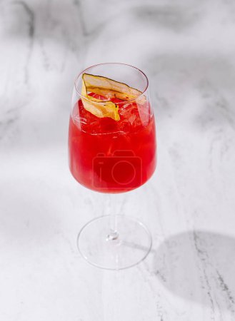 Vibrant red cocktail with ice and citrus garnish, served in a stem glass set on a sleek marble surface