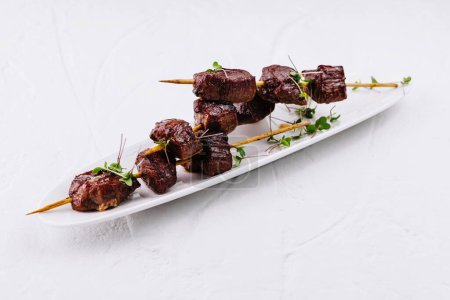 Juicy beef steak cubes on skewers garnished with fresh herbs, served on elegant white platter
