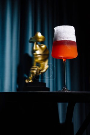 Téléchargez les photos : Un cocktail vibrant dans un grand verre se détache sur un fond sombre et lunatique avec une statue floue - en image libre de droit