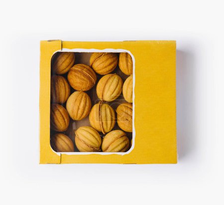 Draufsicht auf köstliche hausgemachte nussförmige Kekse in einer lebendigen gelben Schachtel, isoliert auf weiß