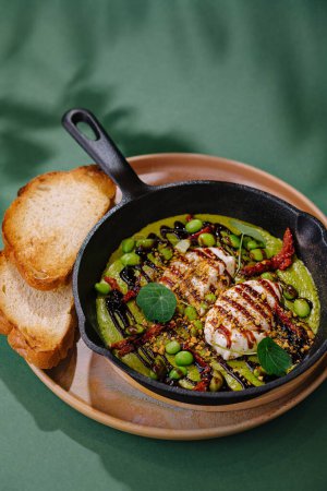 Cast iron skillet with grilled cheese, veggies, and bread on a green background