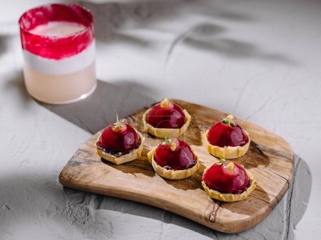 Artistic display of raspberry tarts and a layered beverage on a rustic wooden serving board