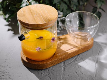 Orange juice in a stylish dispenser with wooden lid, adorned with edible flowers, on a kitchen counter